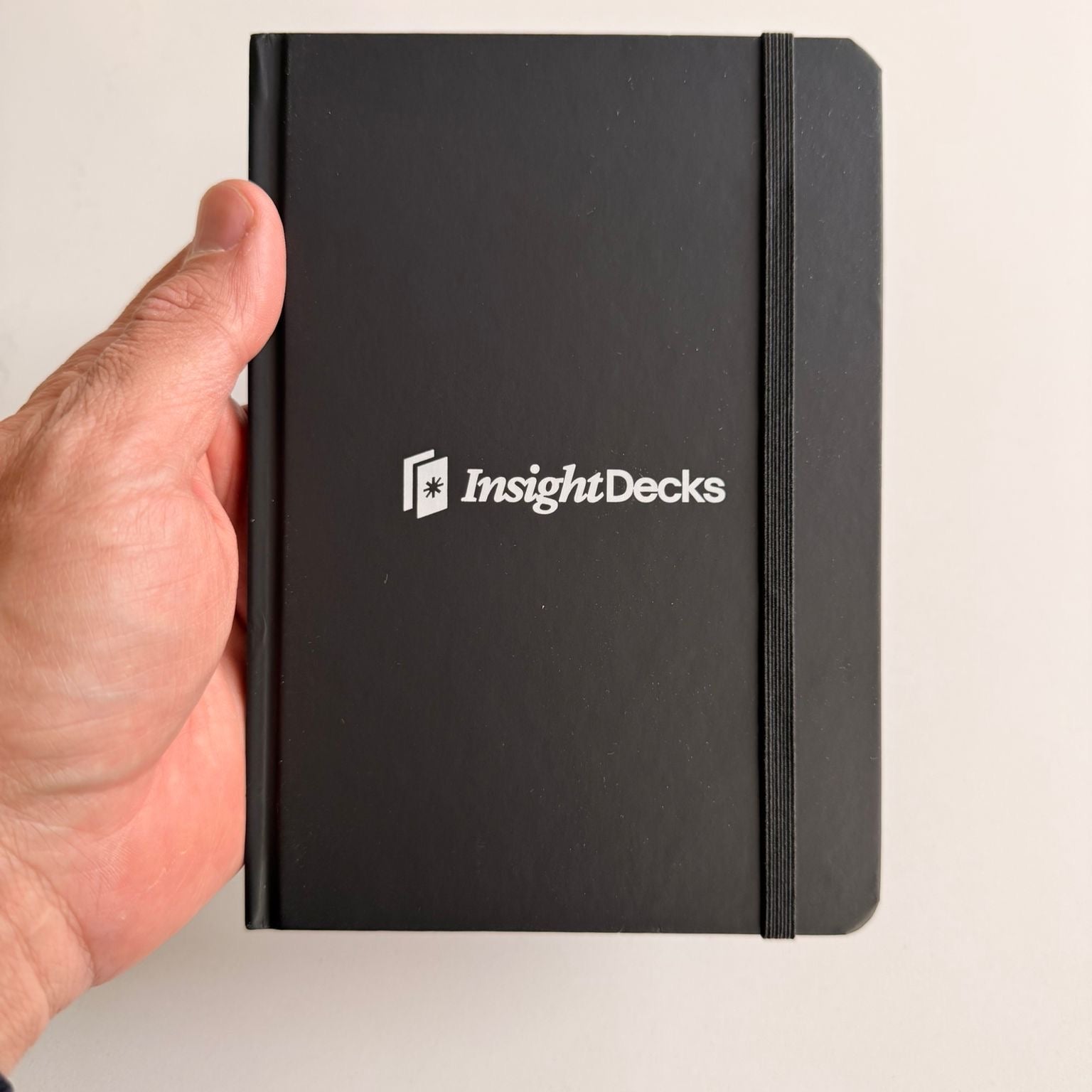 Black notebook with 'InsightDecks' logo held by a hand on a light background
